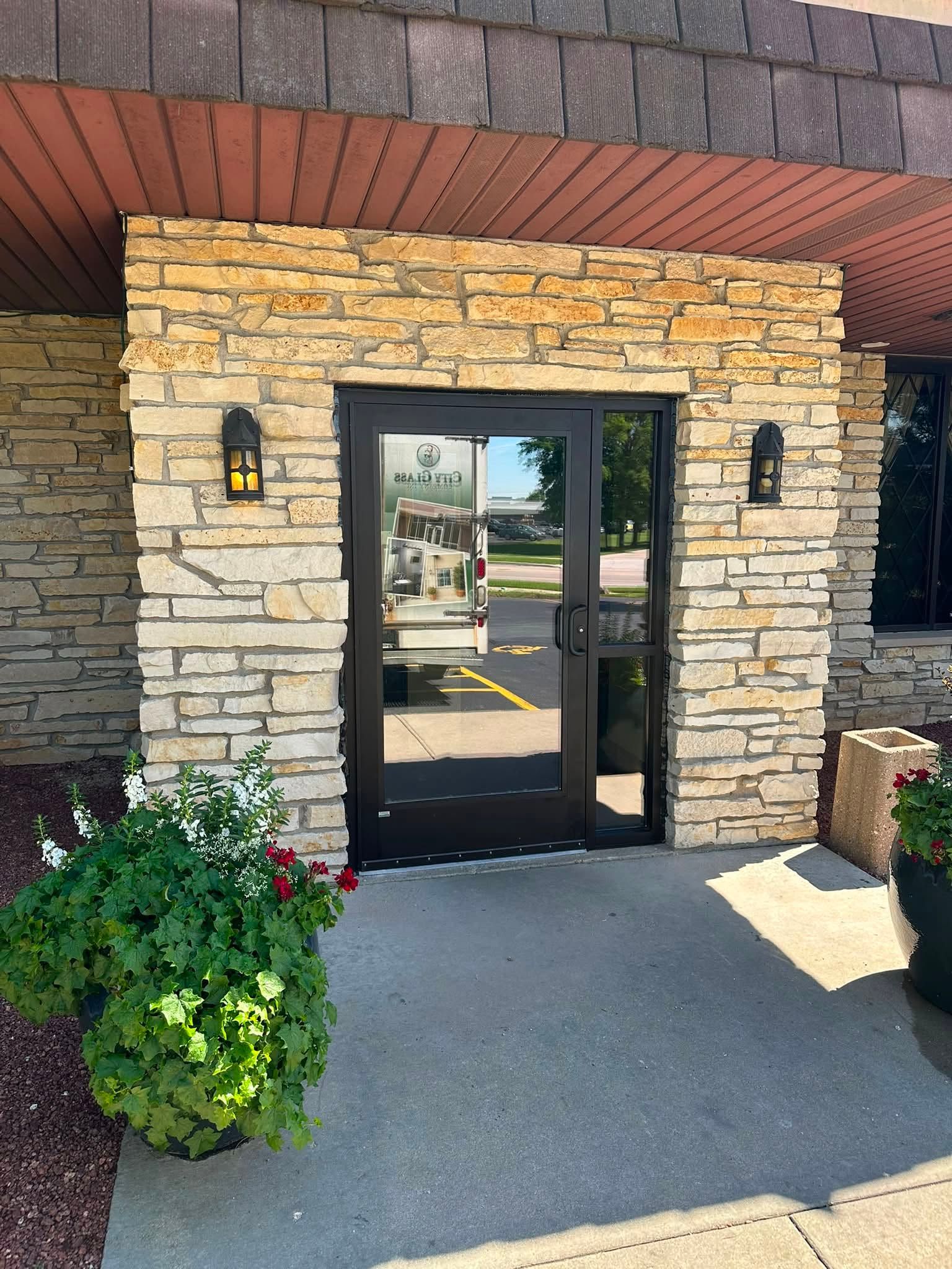 Black commercial glass entry door installed in a stone building exterior in Janesville, WI