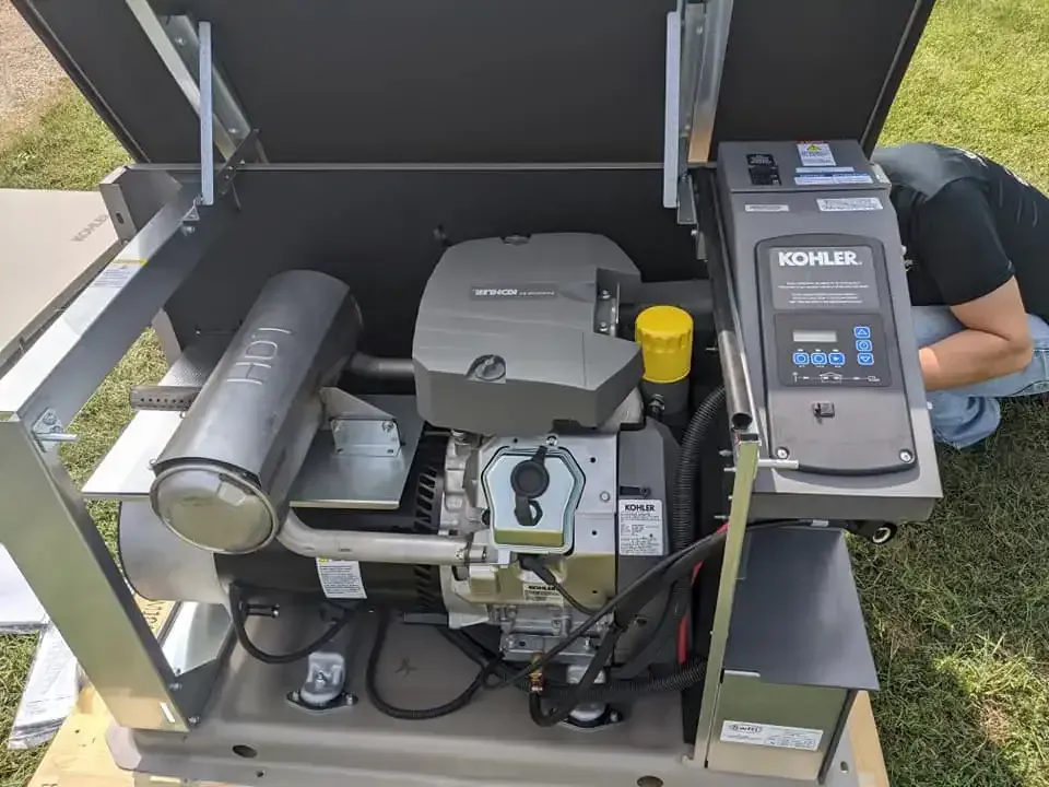 A Kohler home standby generator with its top panel open, outdoors on a wooden pallet as a technician works on it.