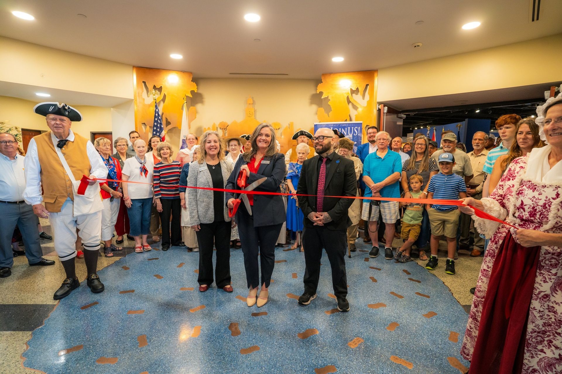 Ribbon-cutting ceremony with a group of people in a lobby, standing behind a red ribbon and applauding.
