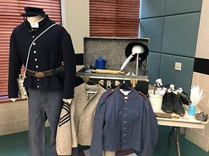 Mannequins displaying historical military-style uniforms and accessories on a table in a museum exhibit