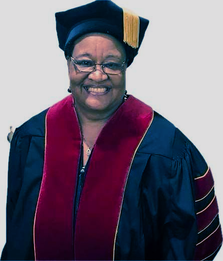Studio headshot of a smiling woman in a black blazer and pearl necklace on a gray background