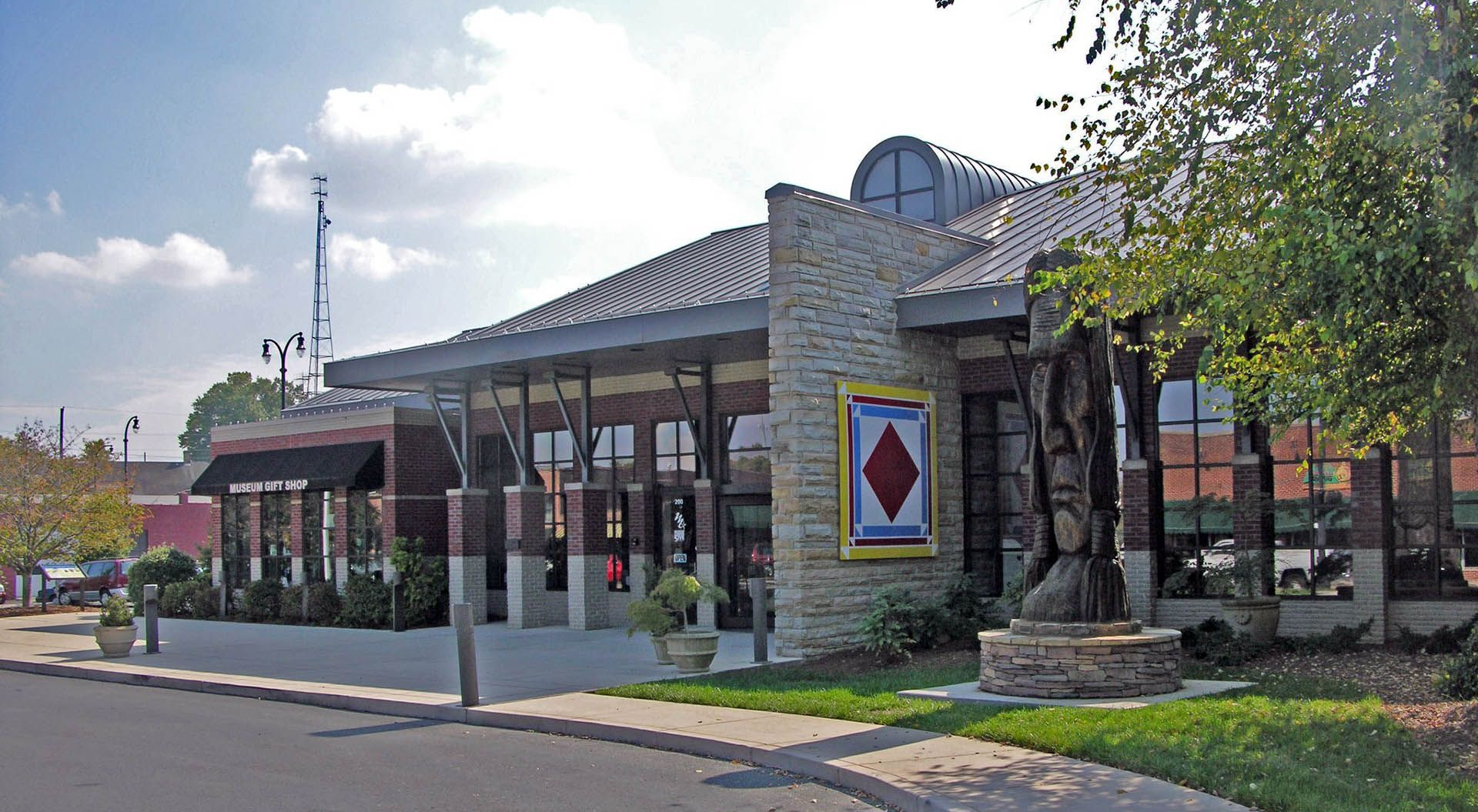 Stone building with glass entrance, tiled roof, and landscaped sidewalk on a sunny street.