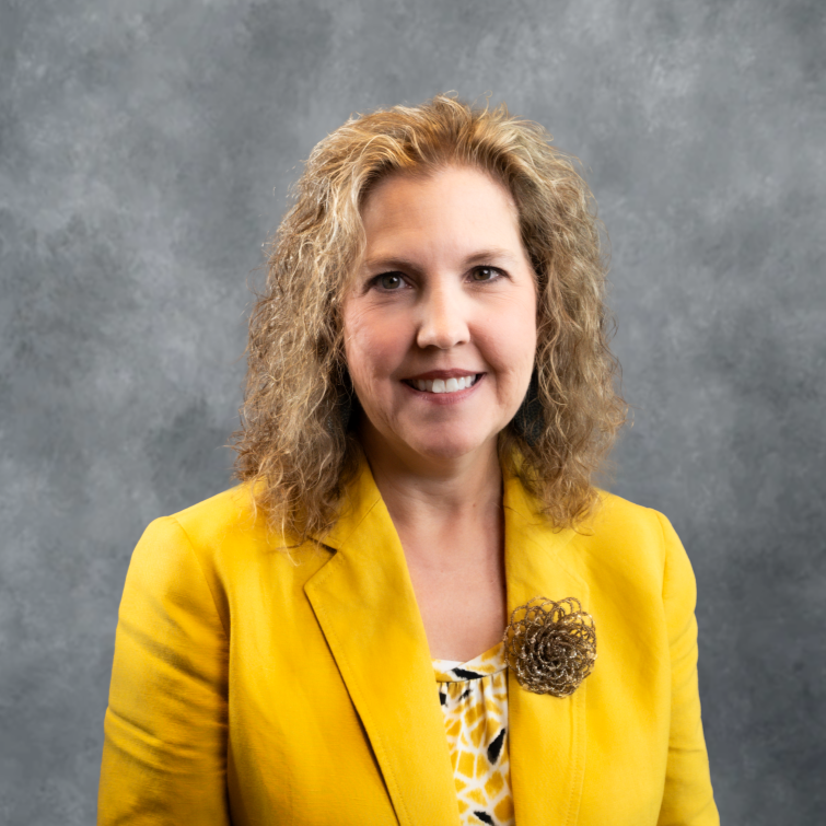 Smiling woman in a bright yellow blazer against a gray studio backdrop