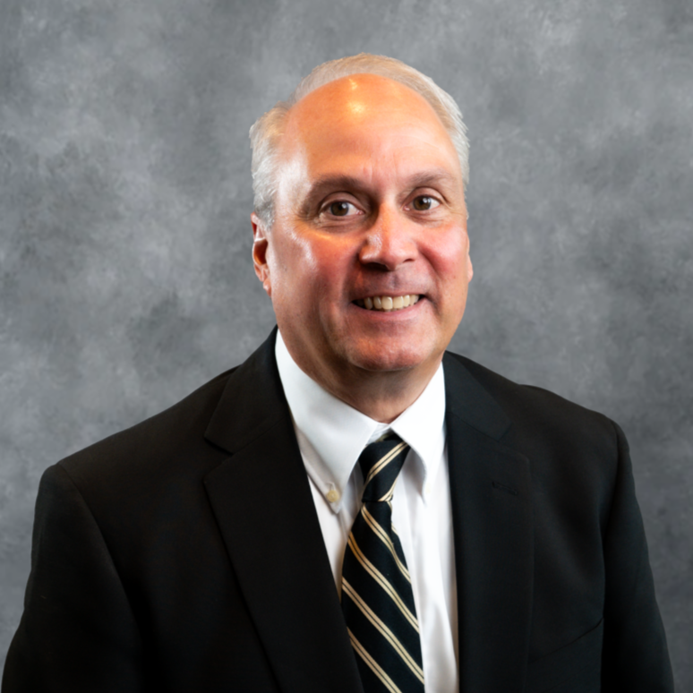 Smiling man in a black suit and striped tie against a gray studio backdrop