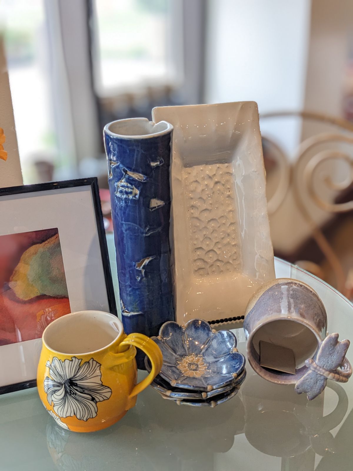 Assorted ceramic mugs and decorative dishes displayed on a glass table