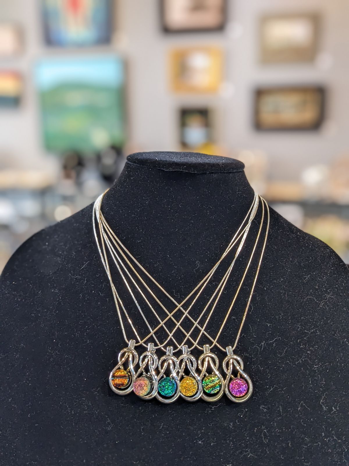 Necklace display with five gold necklaces and colorful gem pendants on a black bust