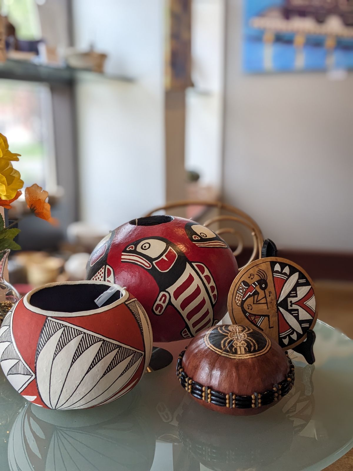 Decorative painted gourds and a small woven basket on a glass table, in red, white, black, and brown patterns