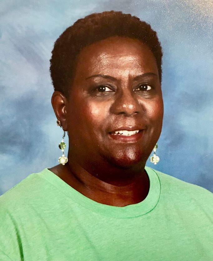 Studio headshot of a smiling woman in a black blazer and pearl necklace on a gray background