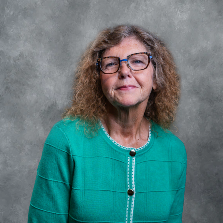 Portrait of a woman in a teal jacket against a gray studio backdrop