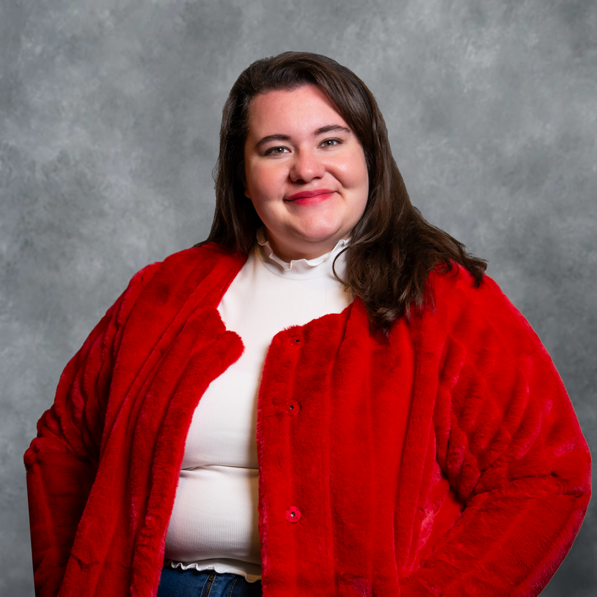 Woman in a red jacket smiling against a gray studio backdrop