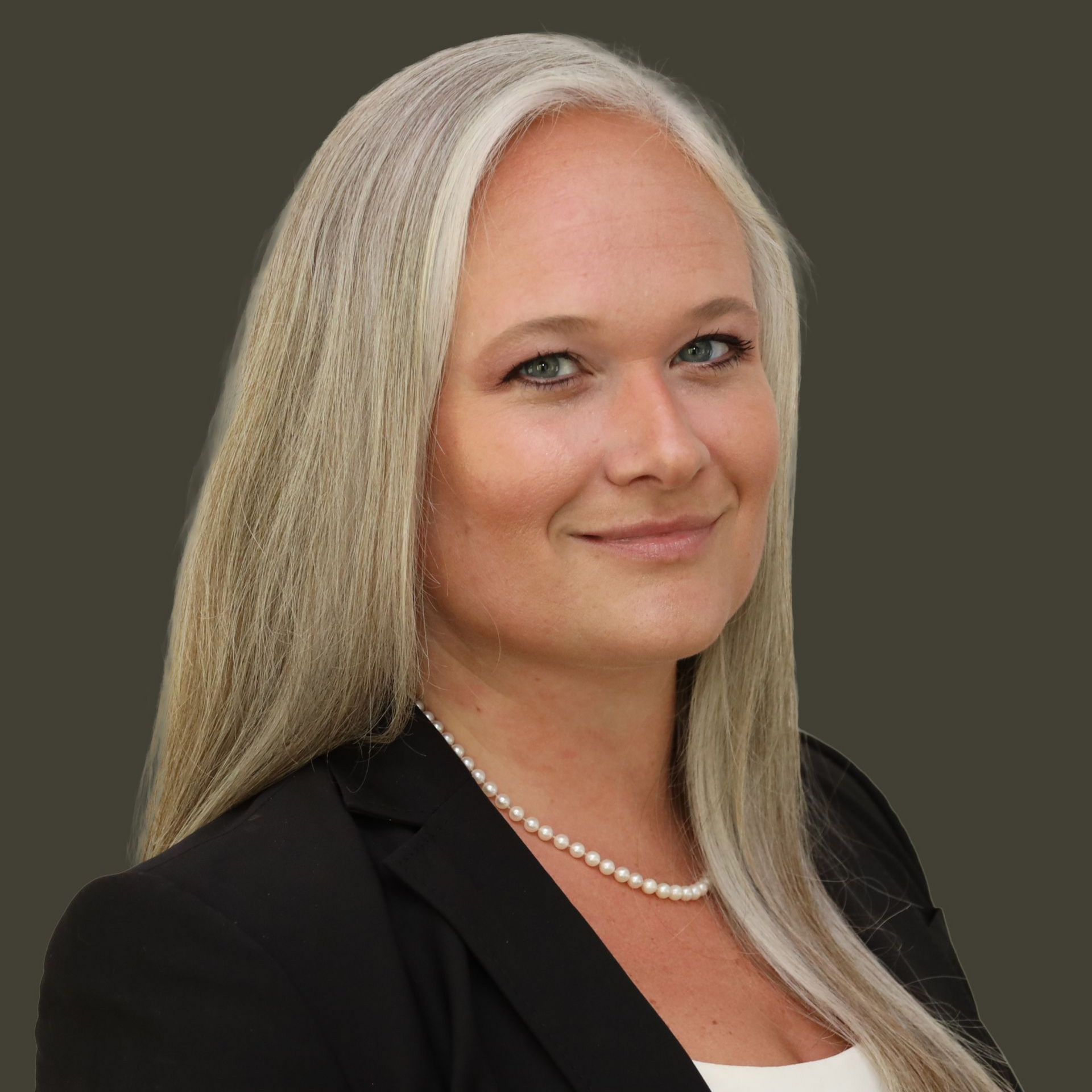 Studio headshot of a smiling woman in a black blazer and pearl necklace on a gray background