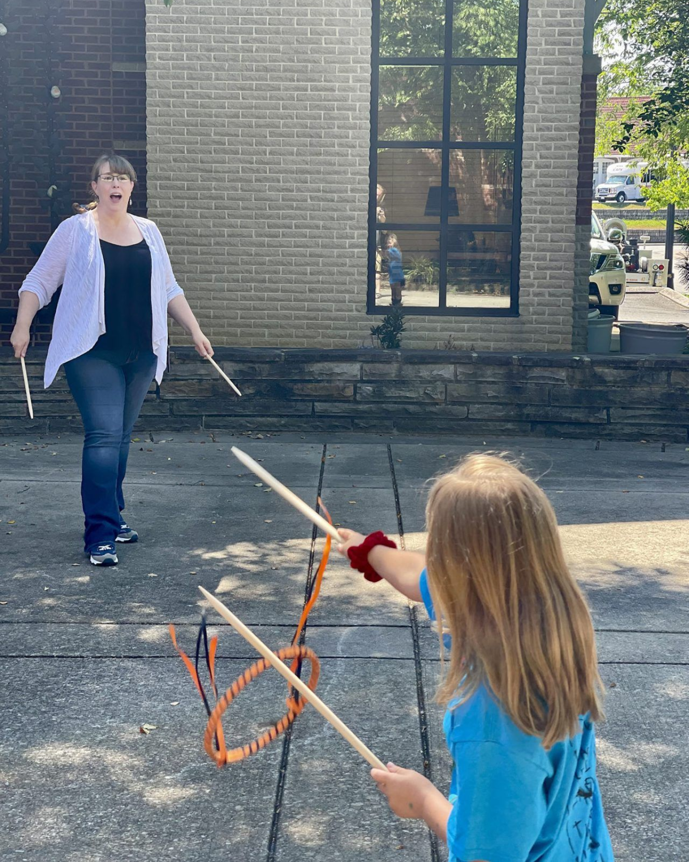 Two people play with toy bows and arrows outside a brick building.