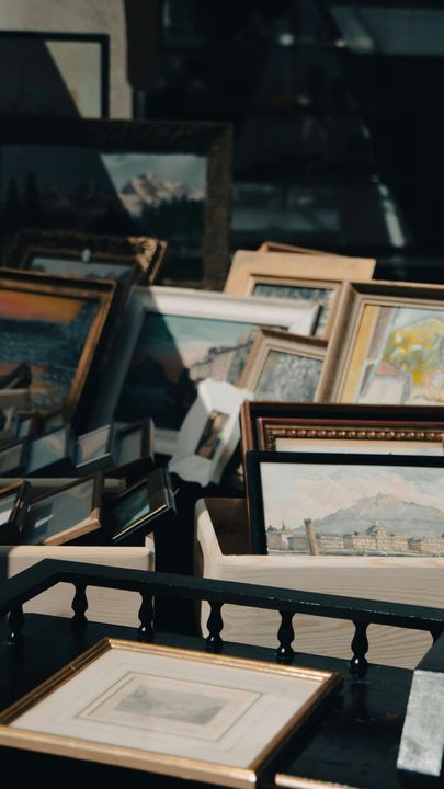 Framed landscape paintings displayed on a table in a dim art market or gallery setting
