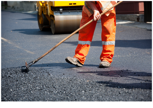 Road worker in orange safety gear repairing asphalt with a tool near a road roller