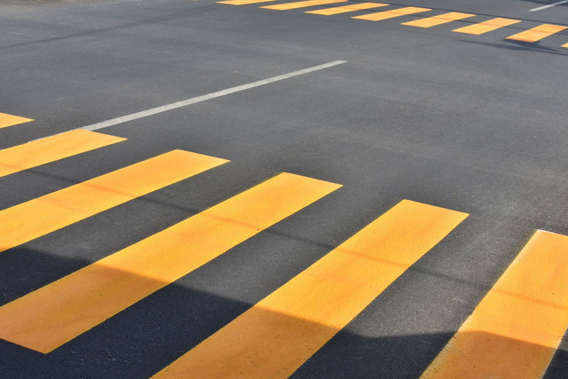 Yellow crosswalk stripes on an asphalt road, viewed at an angle.