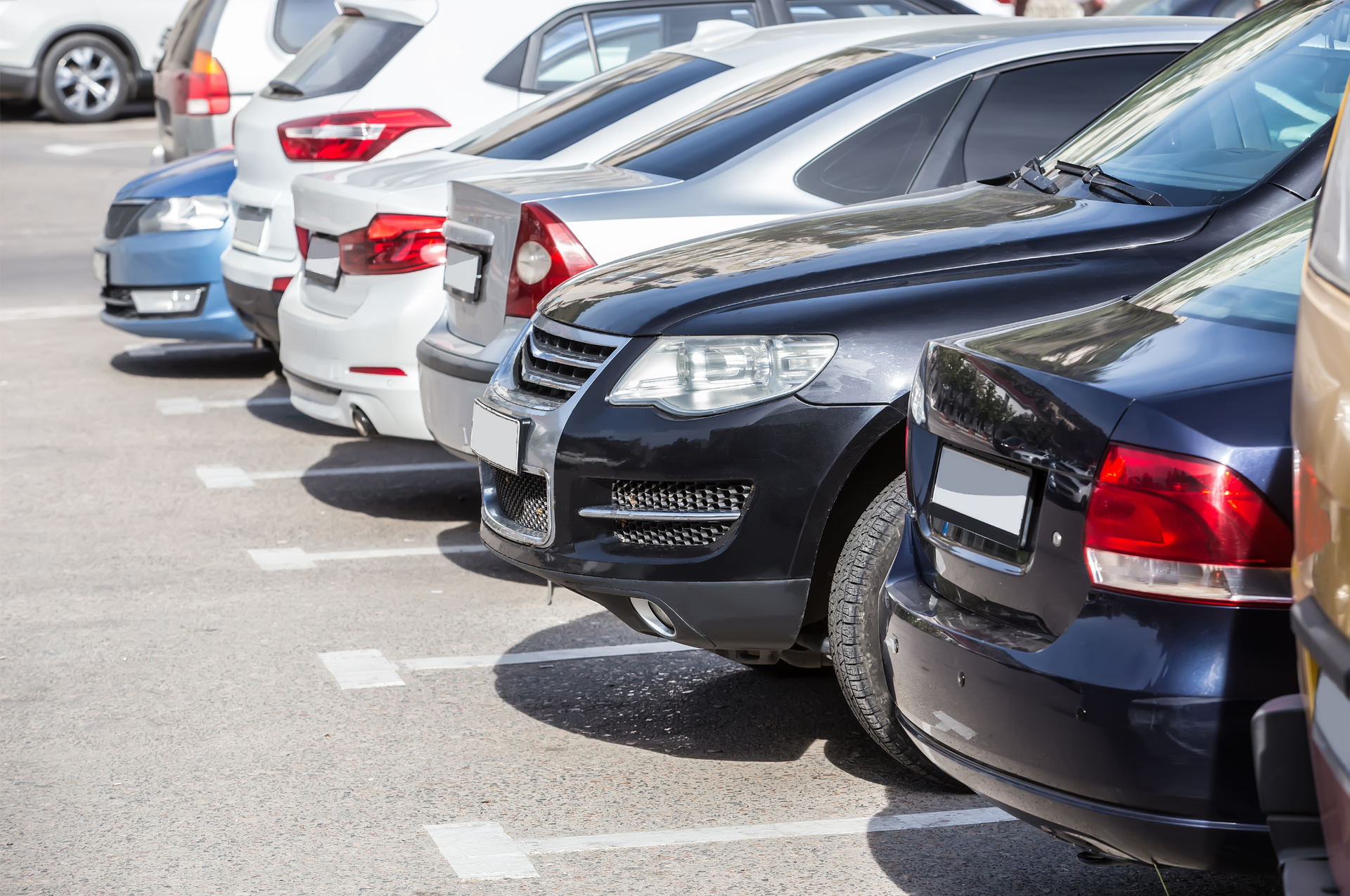 Parked cars lined up in a parking lot, including black, white, and blue vehicles.