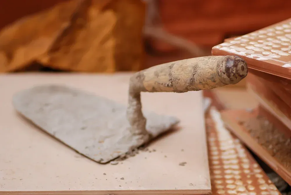 Close-up of a trowel with dried concrete beside a brick or tile surface