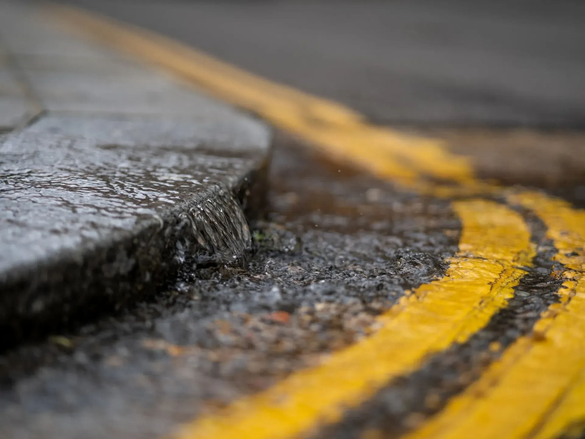 Close-up of a wet asphalt curb with a yellow painted road line bending along the edge