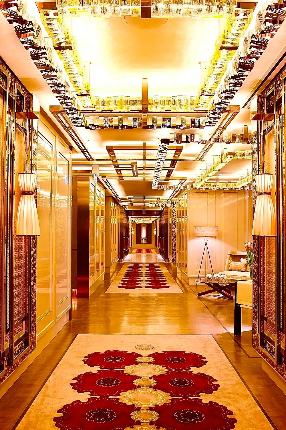 Opulent hotel hallway with gold ceiling lights, mirrored walls, and red floral carpets.