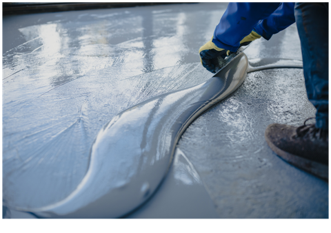 Worker smoothing wet concrete on a reflective surface with a trowel