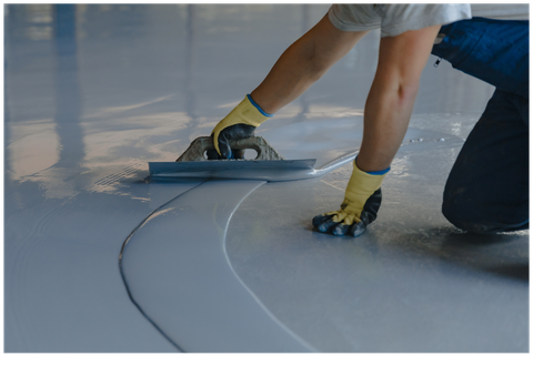 Worker smoothing a glossy gray floor with a hand trowel during installation