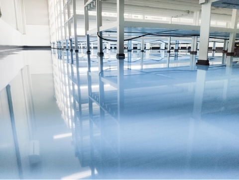 Bright blue polished floor in an empty indoor industrial facility with tables and pillars