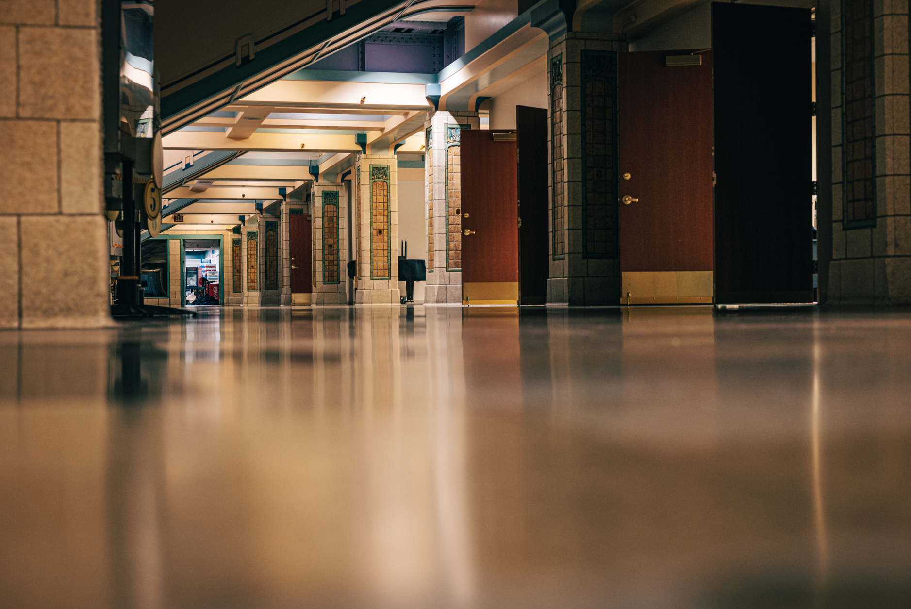 Empty indoor hallway with warm lights, columns, and a glossy floor viewed from ground level