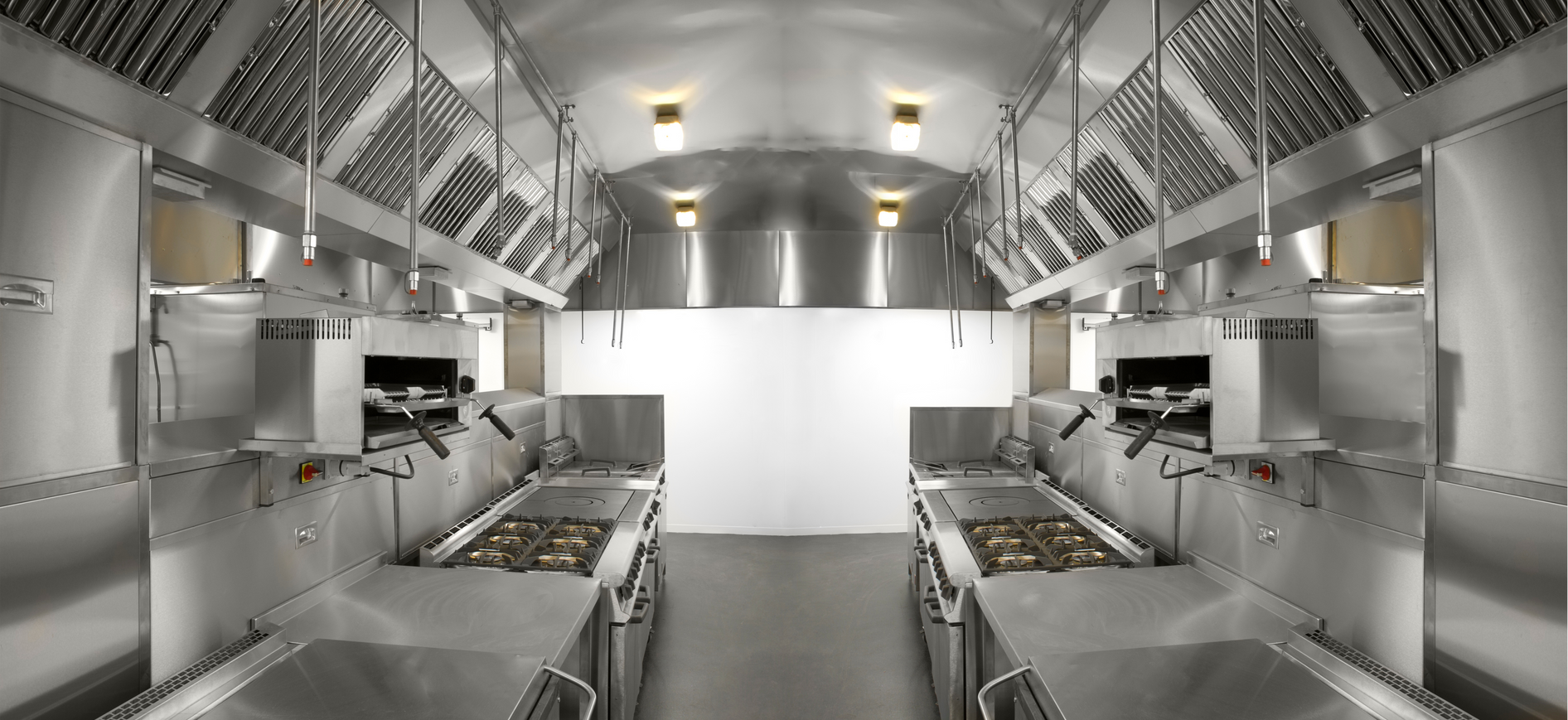 Interior of a stainless-steel kitchen or food prep area with racks, counters, and overhead lights, symmetrical view