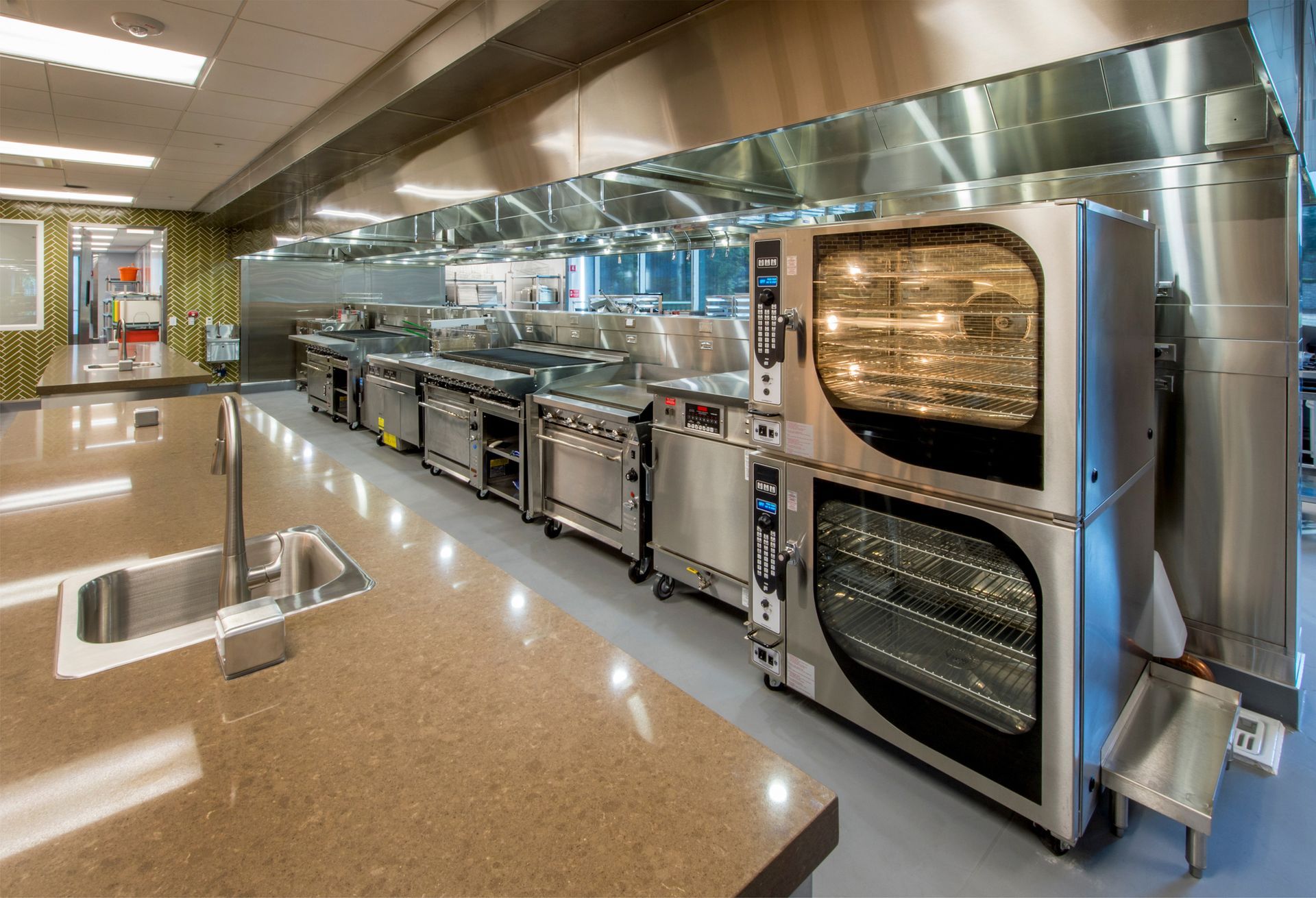 Modern stainless-steel commercial kitchen with ovens, counters, and polished floors