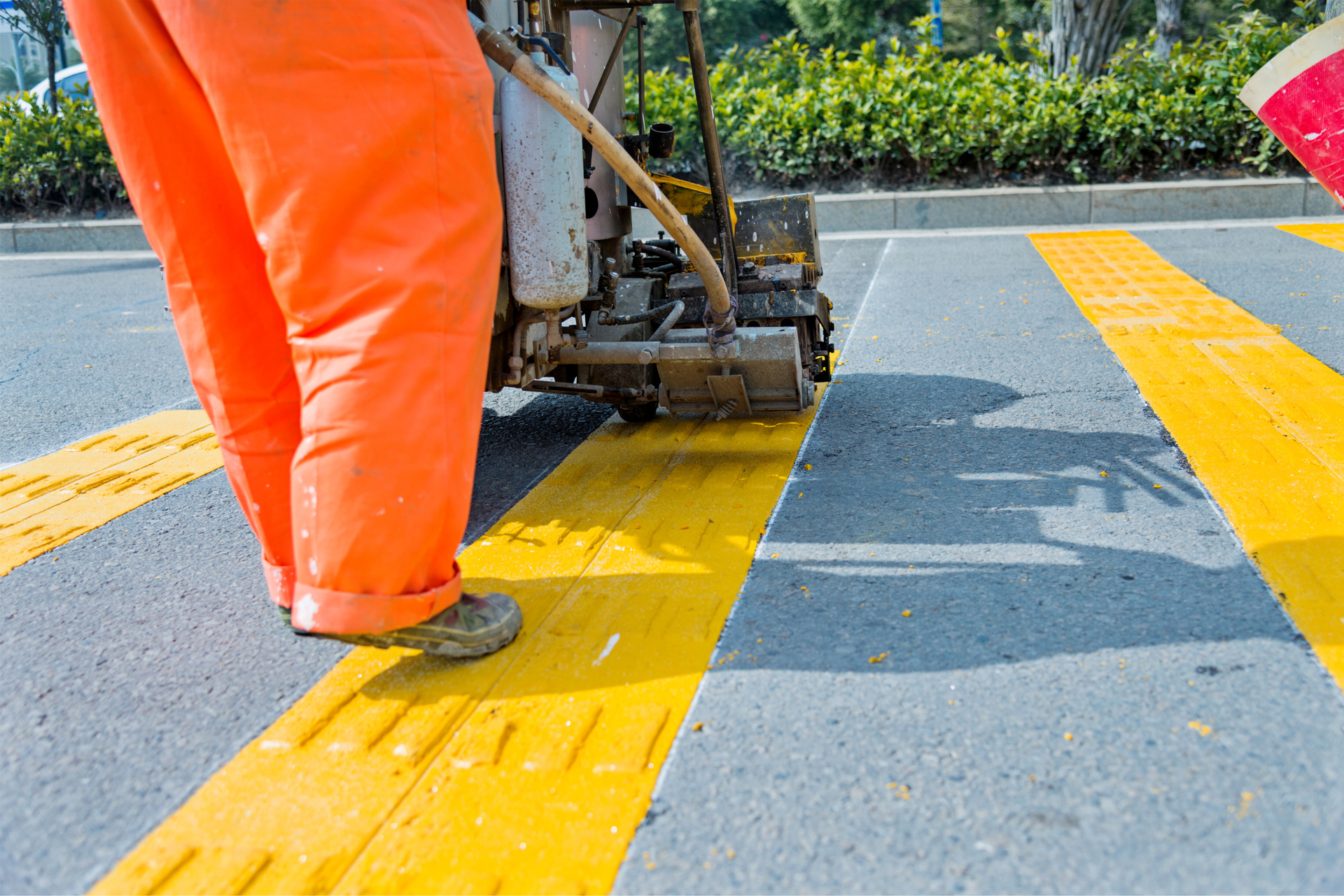 Worker painting a bright yellow road line on asphalt with a striping machine