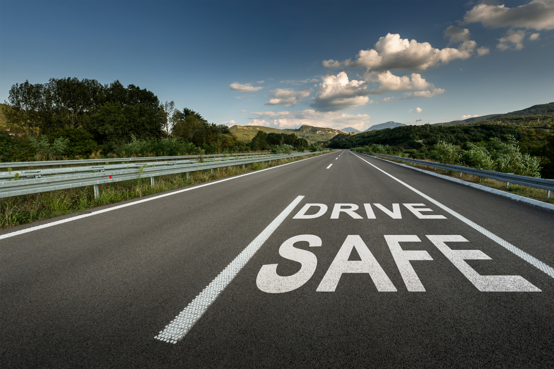 Empty highway with large “DRIVE SAFE” painted on the road under a blue sky with clouds