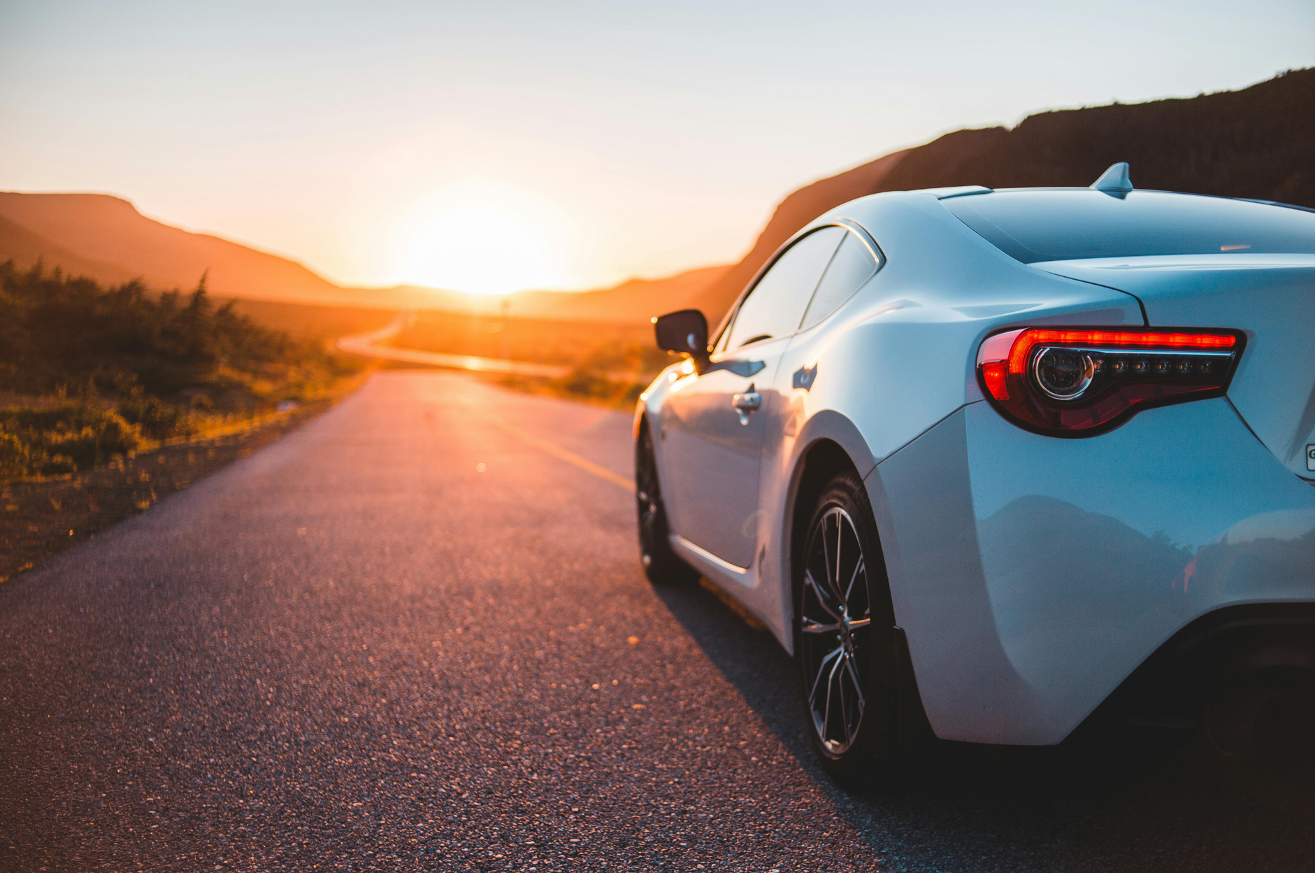 White sports car on a road at sunset, with mountains in the background