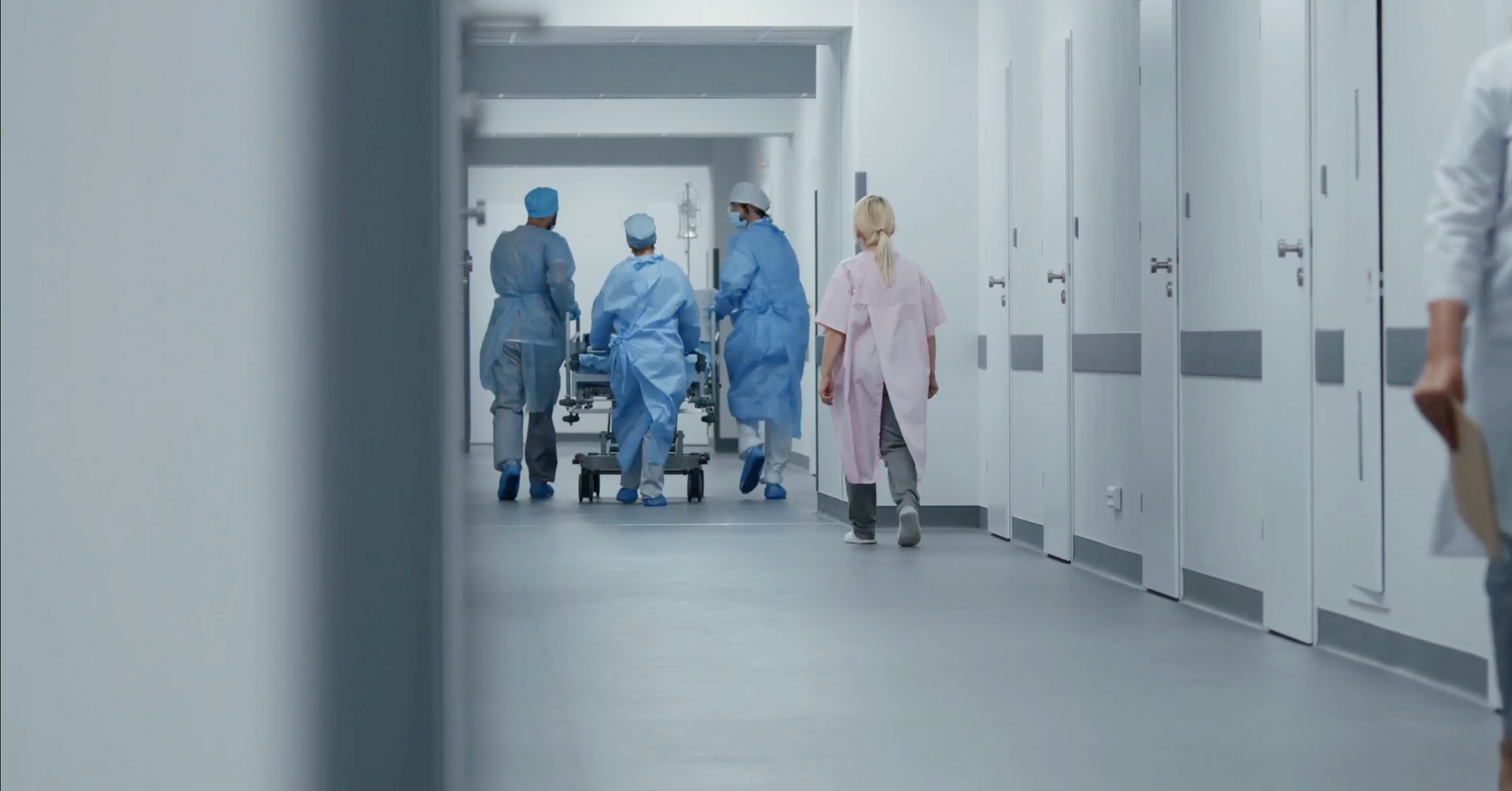 Hospital hallway with staff in blue scrubs and one in pink walking toward the camera