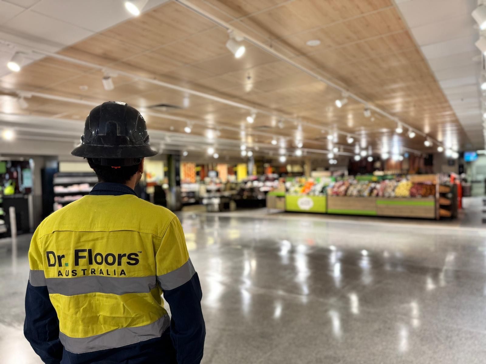 Person in a yellow safety jacket and hard hat stands in a brightly lit store interior.