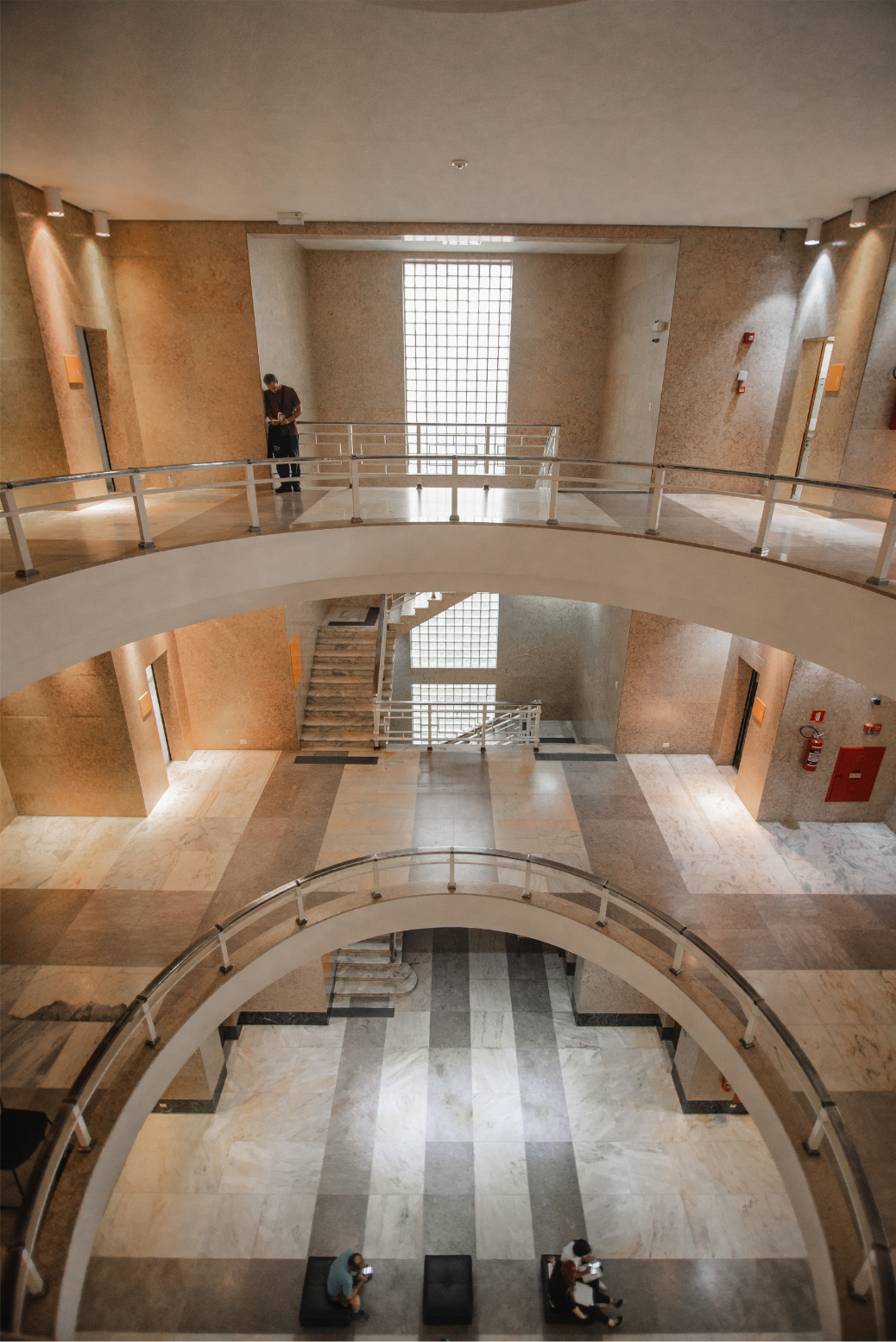Spiral atrium interior with curved balconies, staircases, and a few people seated on the ground floor.