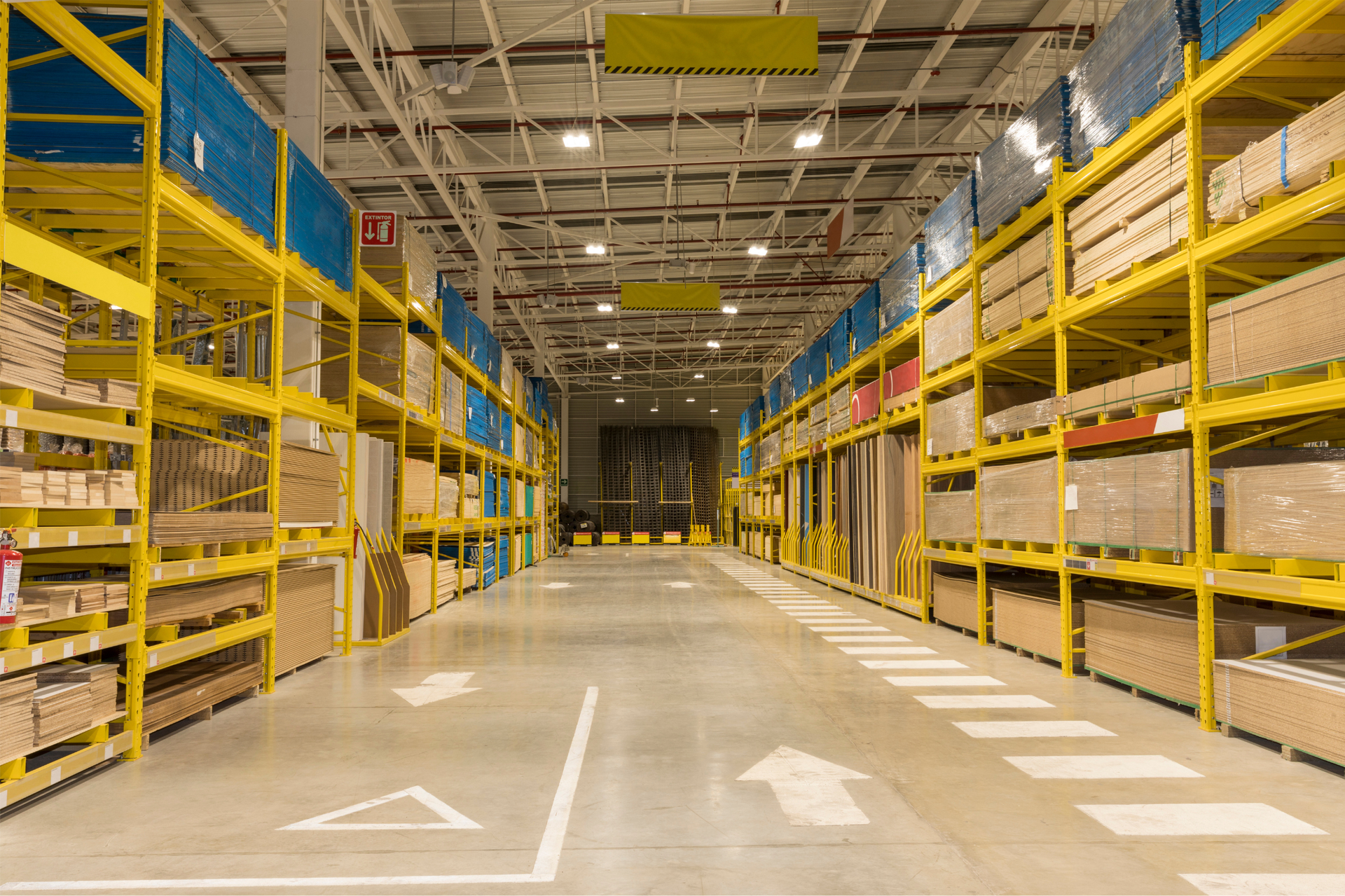 Aisle in a large warehouse with yellow shelving and marked floor lanes.