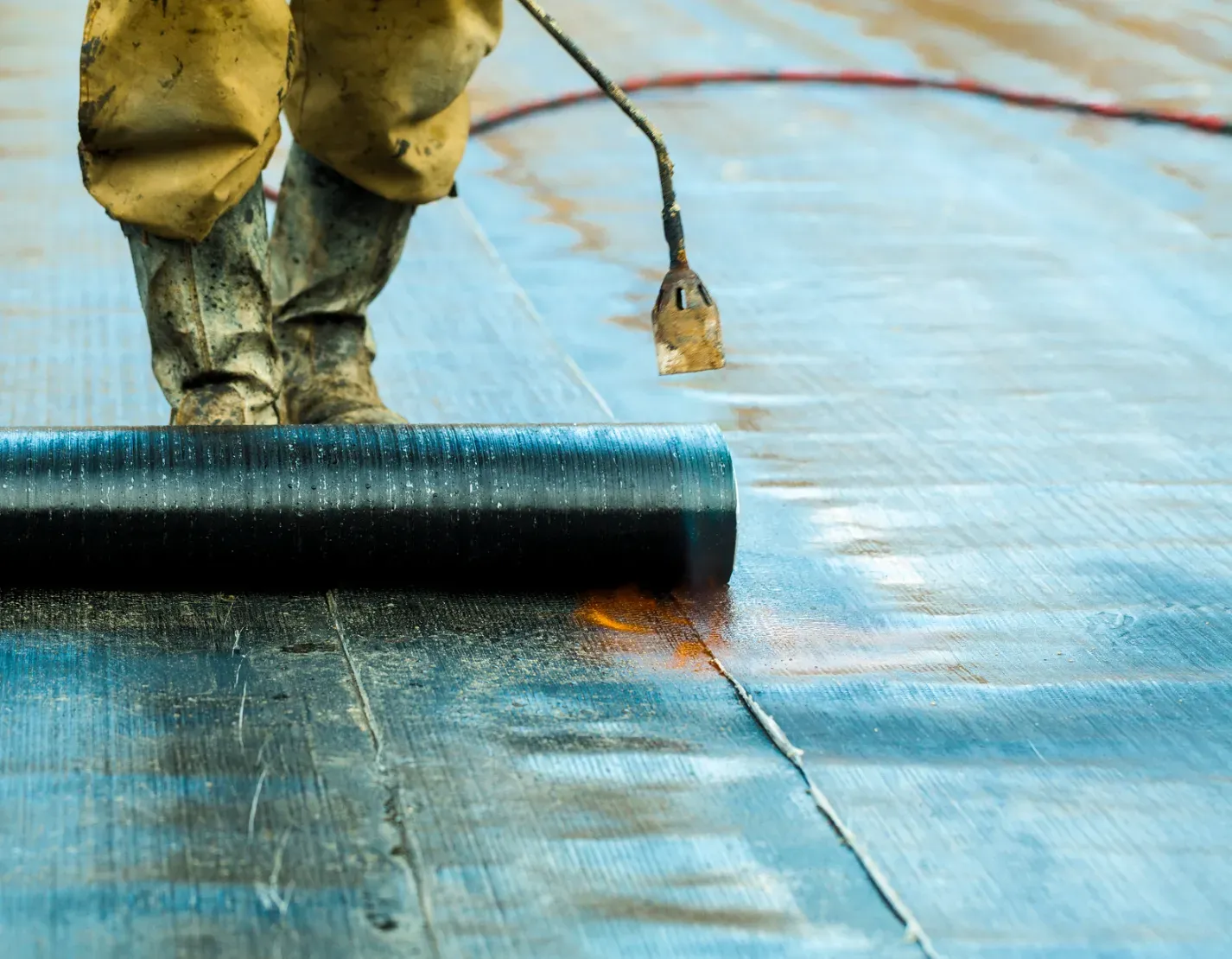 Worker rolling black waterproofing material over a blue rooftop surface