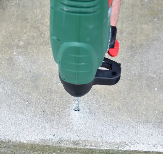 Green power drill bit drilling into a concrete surface