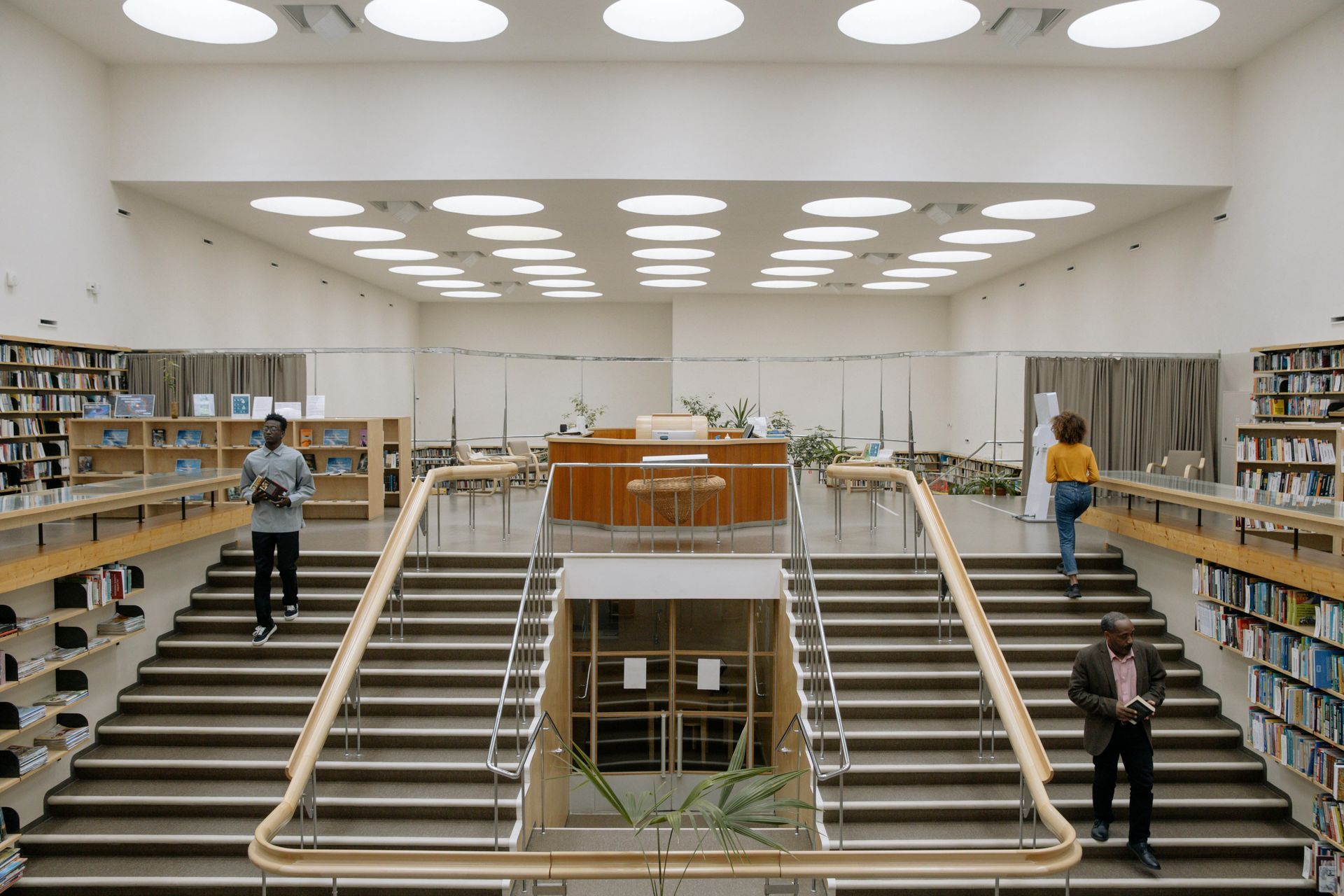 Spacious library atrium with wide staircases, bookshelves, and a few people browsing on both sides