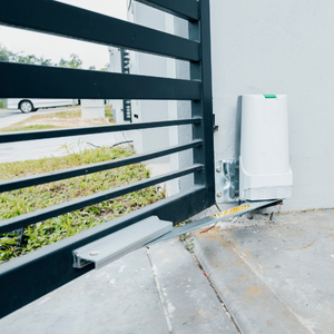 Automatic gate with motor attached to a concrete wall; black metal gate, grass, overcast.