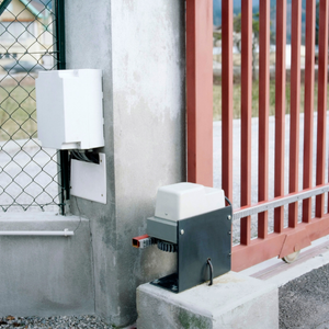 Automatic gate opener system attached to a red metal gate and concrete pillars.