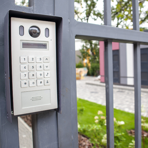 Silver intercom panel with keypad, camera, and speaker mounted on a black metal gate.