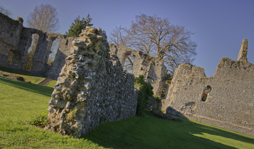 Ruins of a stone castle wall on a grassy hillside under clear blue sky