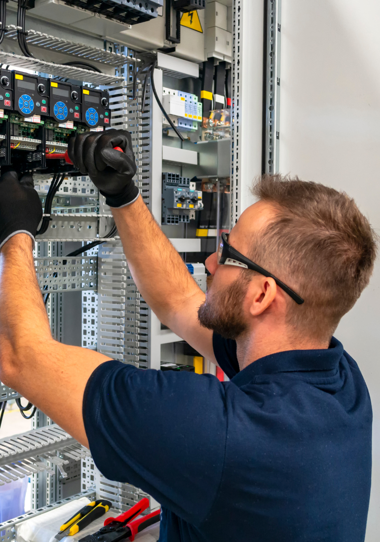 Electrician working inside an electrical panel, wearing safety glasses and gloves.