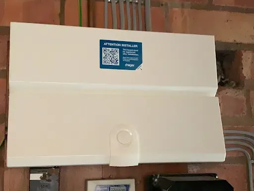 White rectangular electrical box mounted on a brick wall with conduits above and electrical components below.