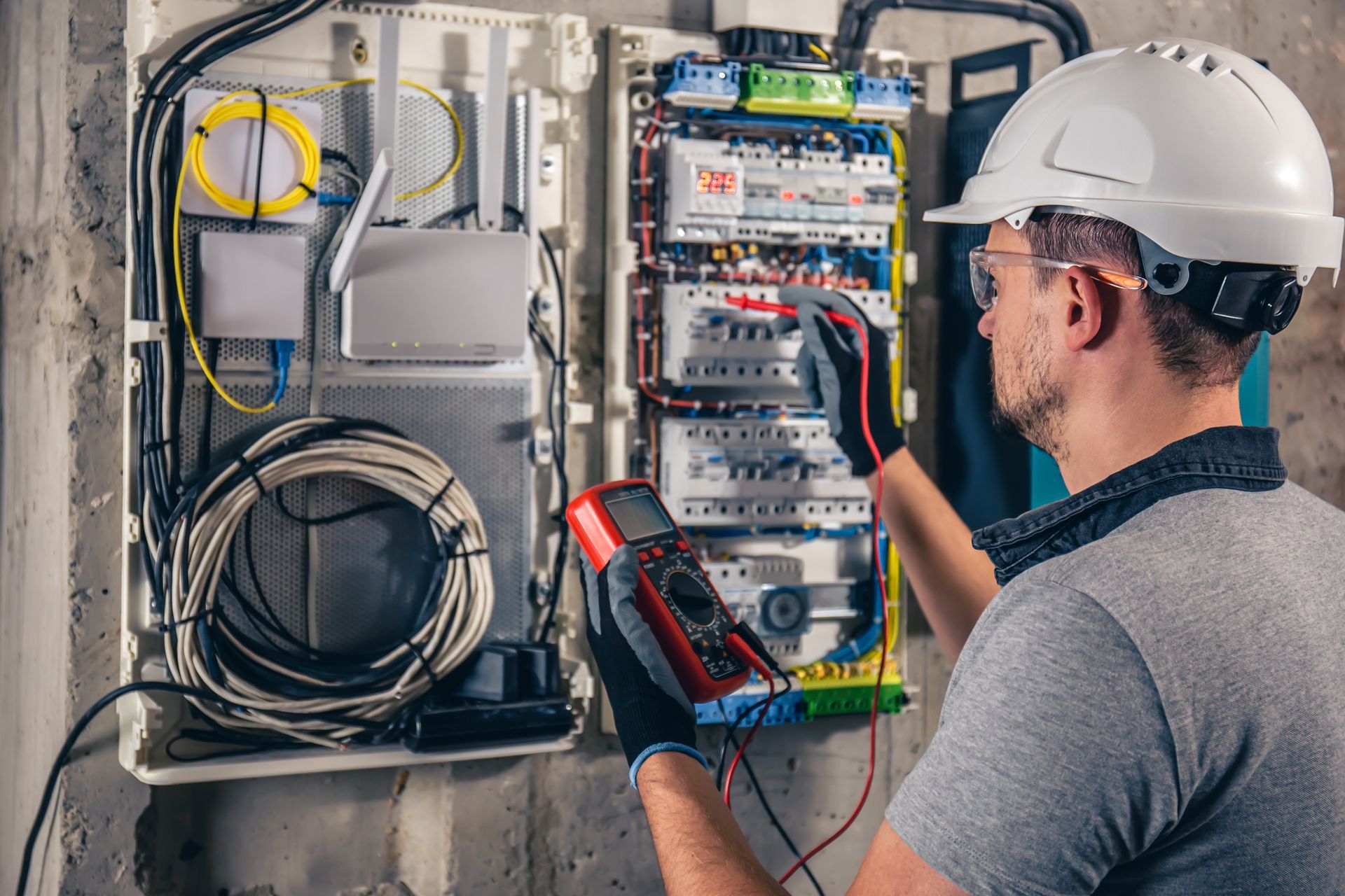 Electrician in hardhat using multimeter on electrical panel.
