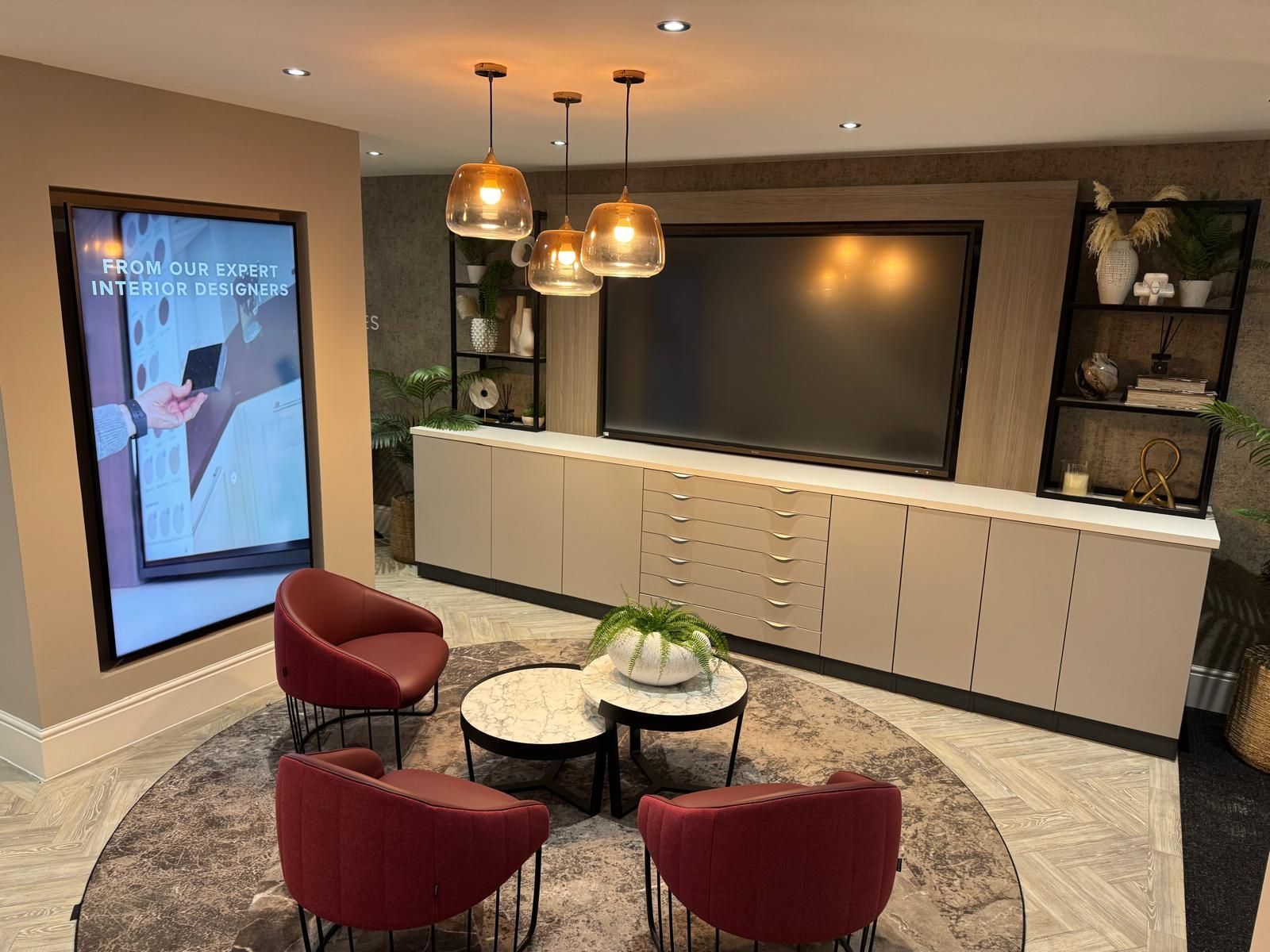 Modern lounge with large TV, white cabinets, round rug, red chairs, and hanging pendant lights