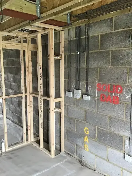 Interior of a building under construction, showing wooden frame, concrete block wall, electrical wiring, and markings.