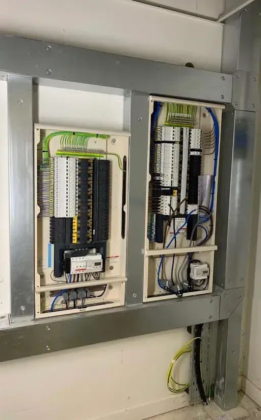 Electrical control panels mounted inside a metal frame on a wall, with wires, breakers, and terminals.