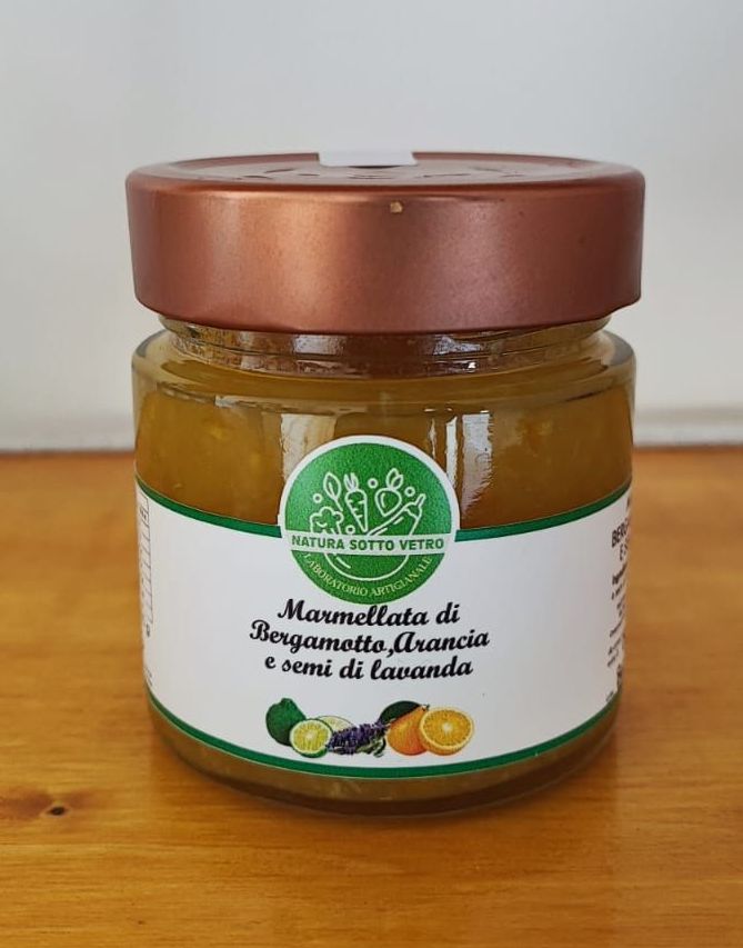 Un vasetto di marmellata marrone con coperchio in rame ed etichetta bianco-verde su una superficie di legno.